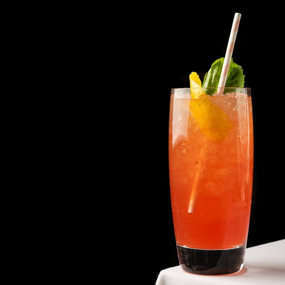 Pink-red cocktail with citrus peel and herbs